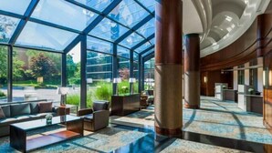 A spacious lobby with a glass facade, wooden columns, and a patterned carpet. - The Westin Waltham-Boston (Waltham)