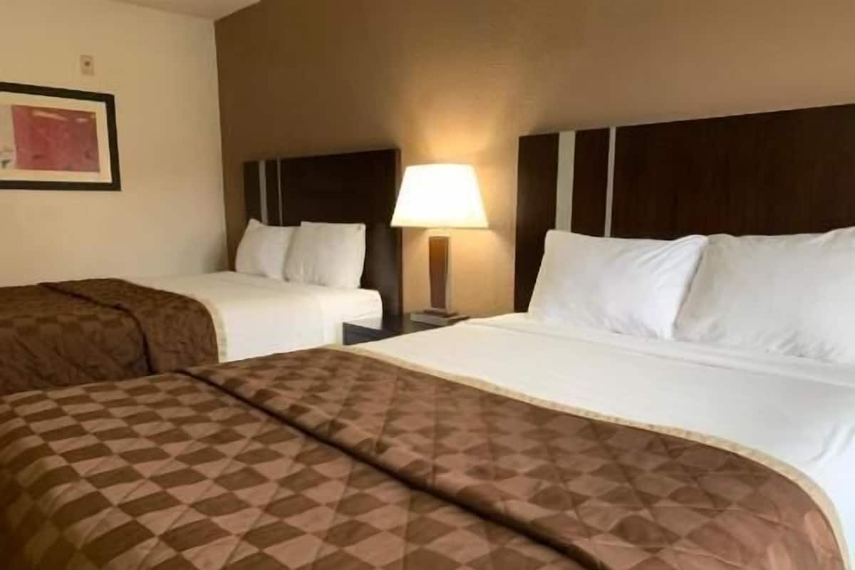 A hotel room with two beds, a nightstand with a lamp, and a framed picture on the wall.