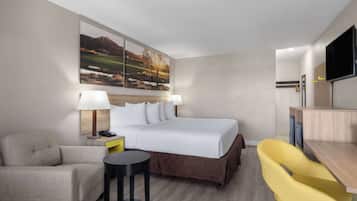 A hotel room with a bed, a desk, a chair, a small table, and a painting on the wall.