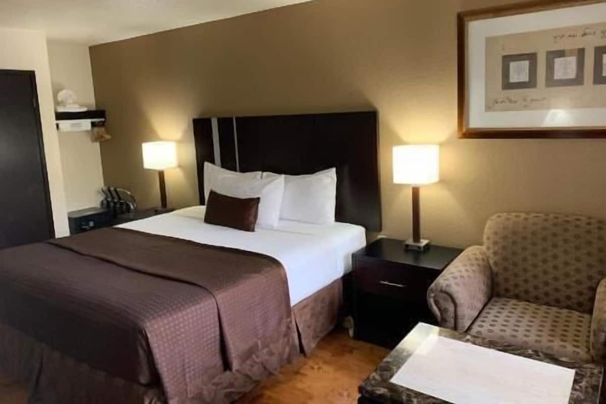 A hotel room with a large bed, two bedside lamps, a nightstand, a chair, and a framed picture on the wall.