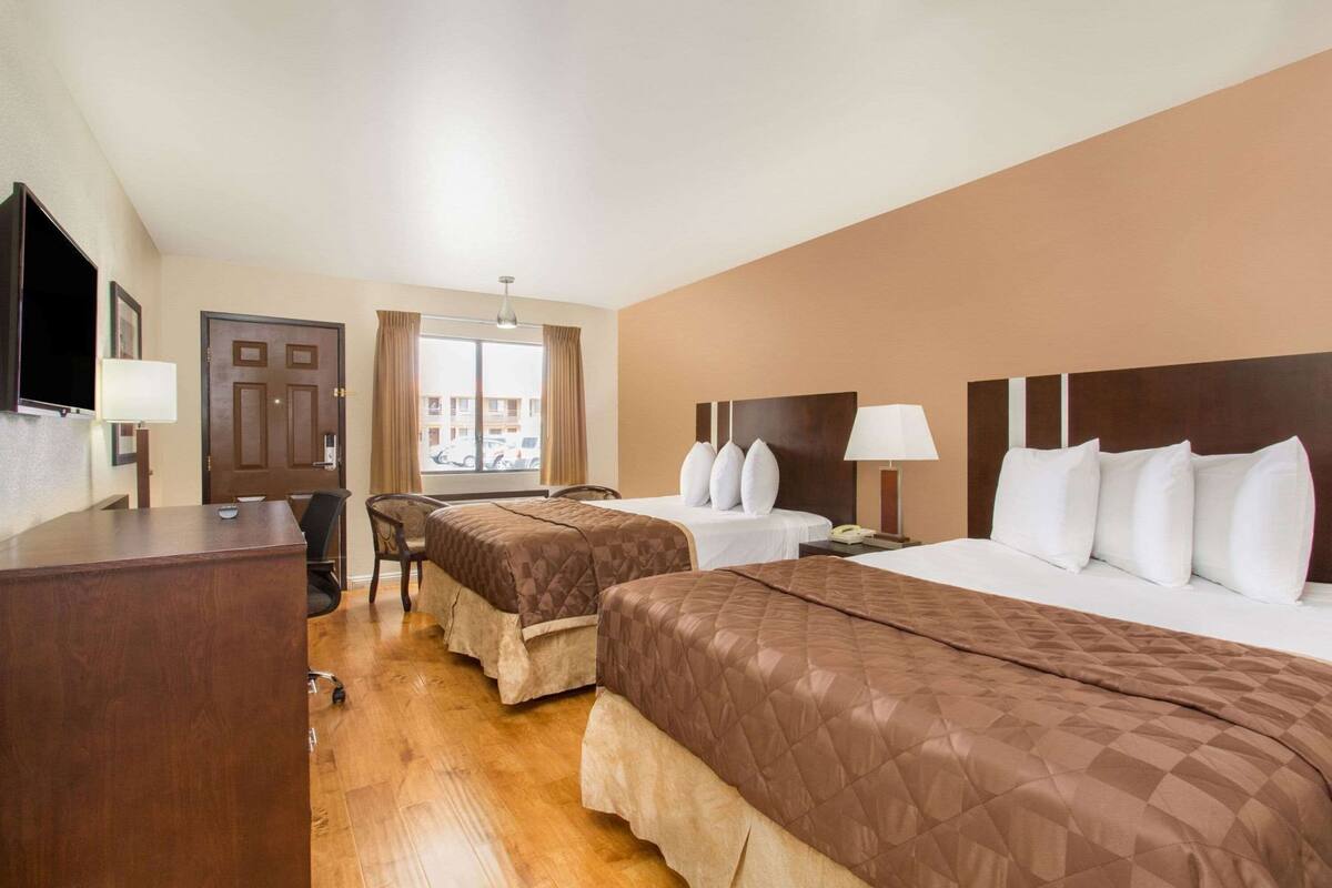 A hotel room with two beds, a desk, a chair, a TV, and a window with curtains.