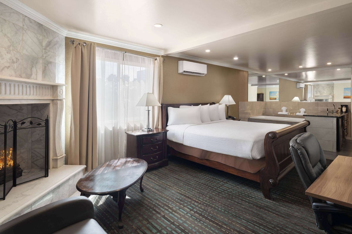 A hotel room with a bed, bedside table, lamp, chair, and a fireplace.