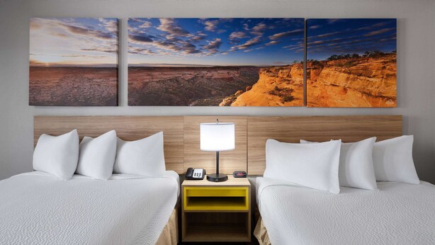 A hotel room with two beds, a nightstand with a lamp, and a wall-mounted painting of a desert landscape. - Days Inn by Wyndham Las Vegas Airport Near the Strip (Las Vegas)