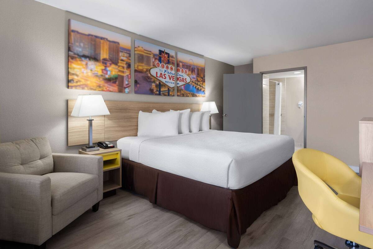 A hotel room with a bed, a desk, a chair, and a wall with a Las Vegas sign.