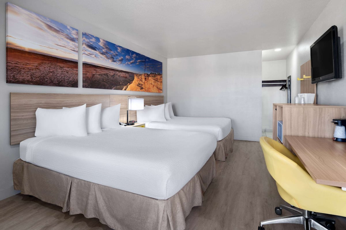 A hotel room with a large bed, two bedside tables, a desk with a chair, a flat-screen TV, and two wall-mounted paintings.