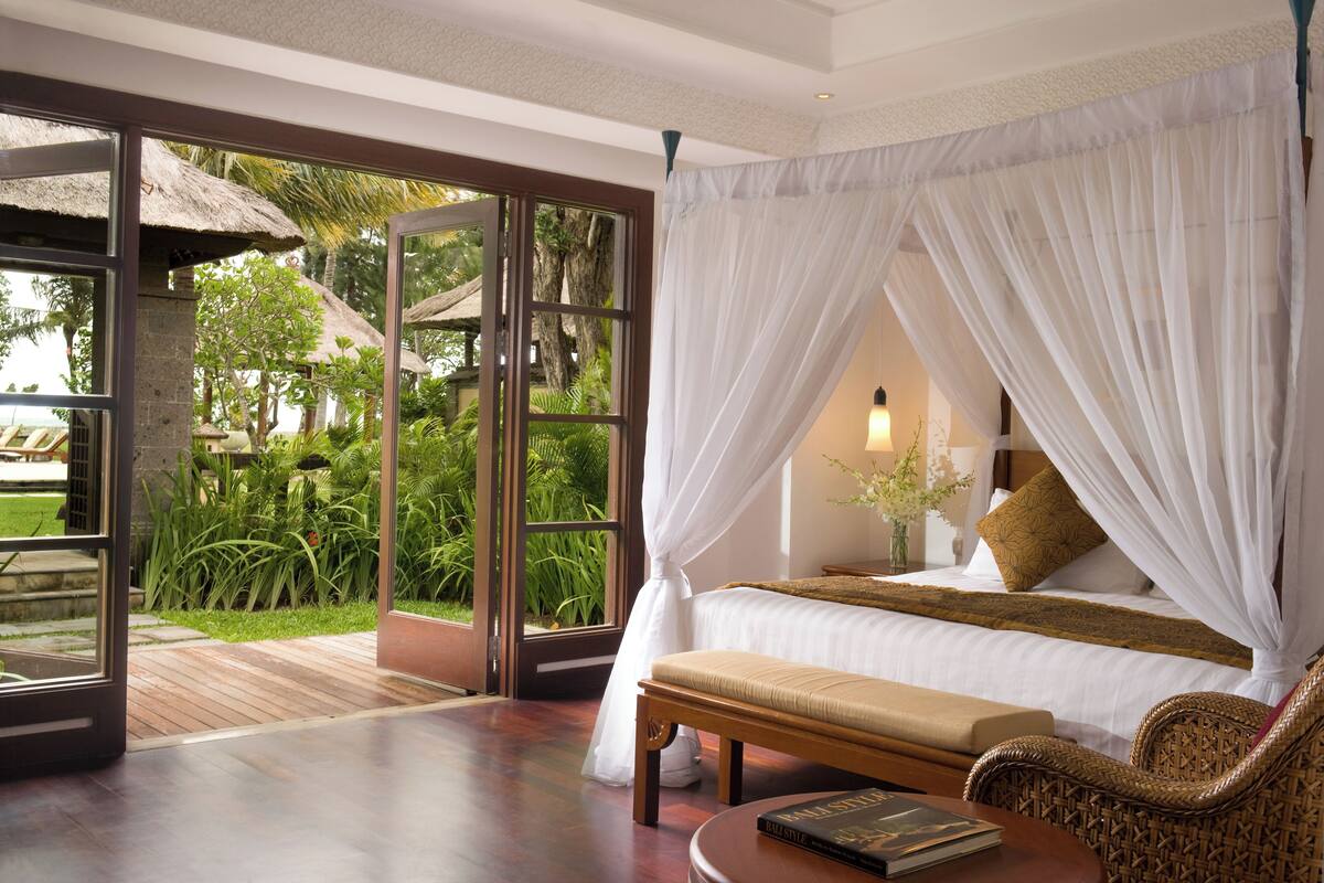 A spacious bedroom with a large bed, a bench, and a wicker chair.