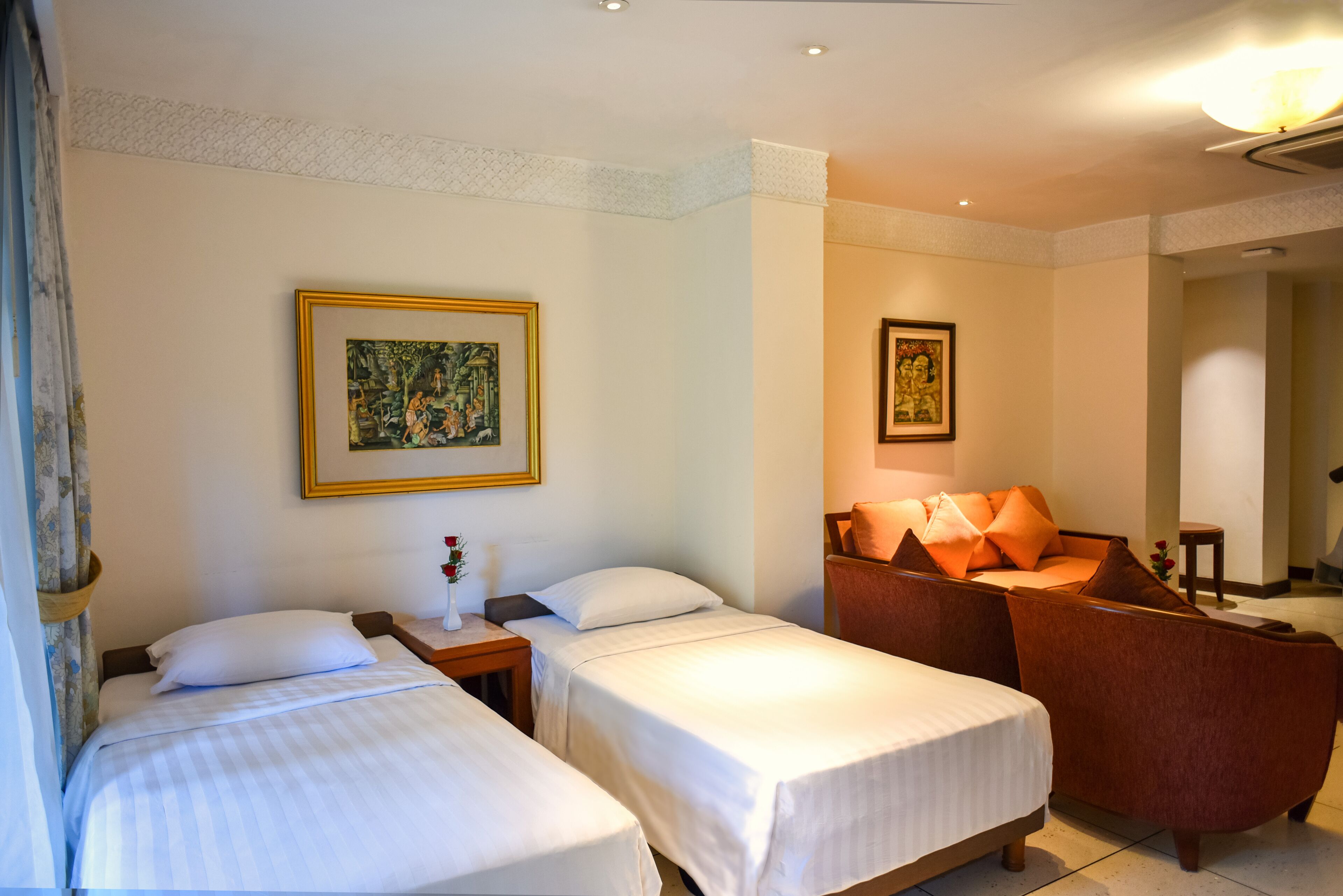 A hotel room with two single beds, a sofa, and two framed artworks on the walls.