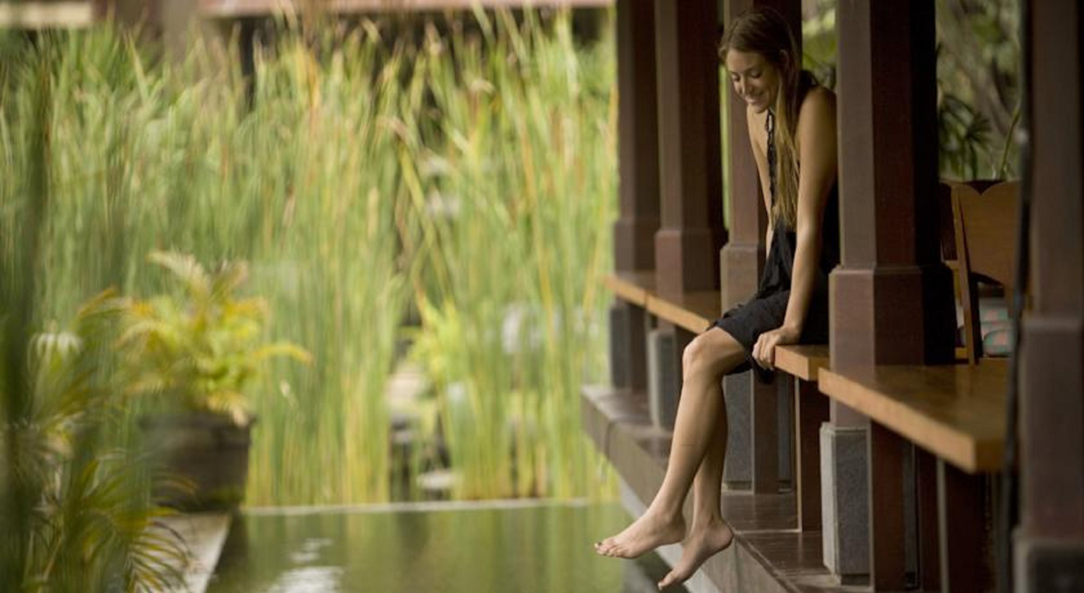 A person sitting on a wooden bench in a serene indoor garden with tall plants and a water feature.