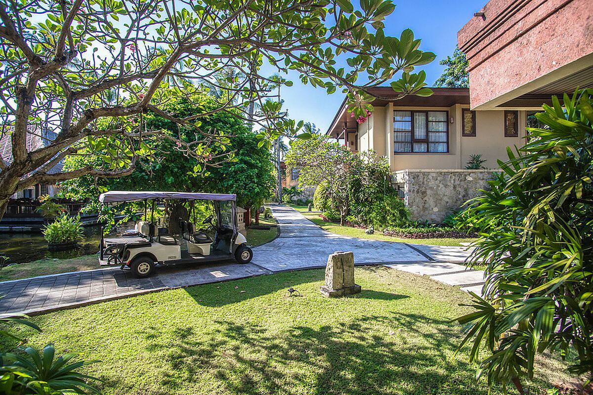 A golf cart parked on a paved driveway leading to a house with a stone wall and lush greenery.