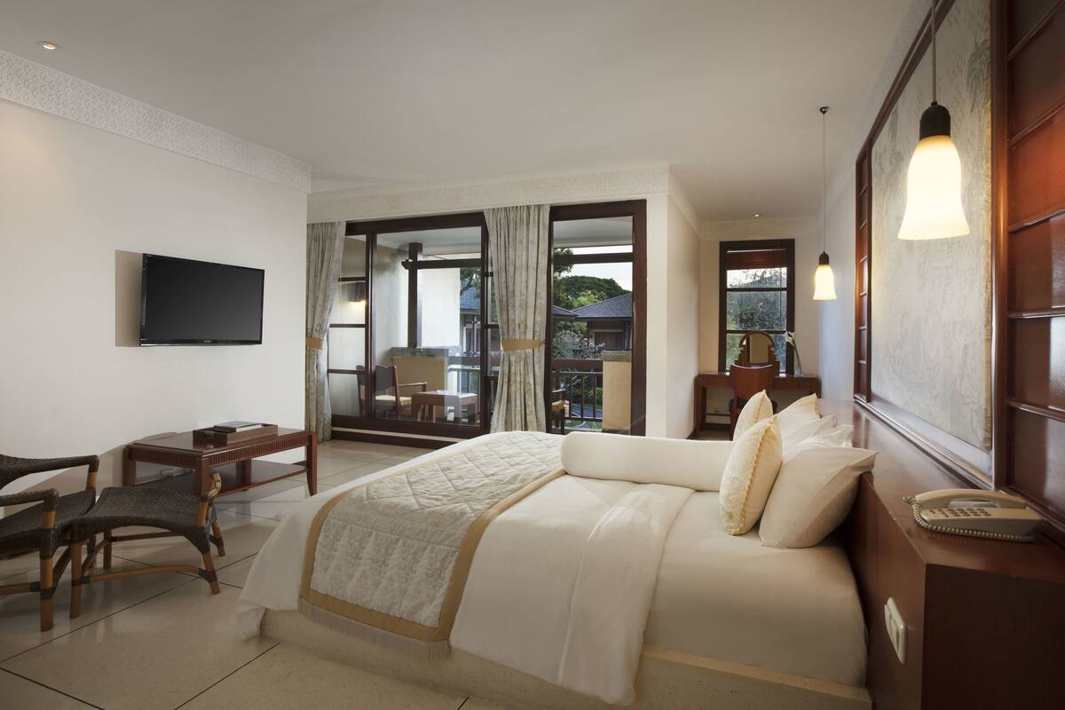 A hotel room with a large bed, a desk, a chair, a television, and a view of the outdoors.