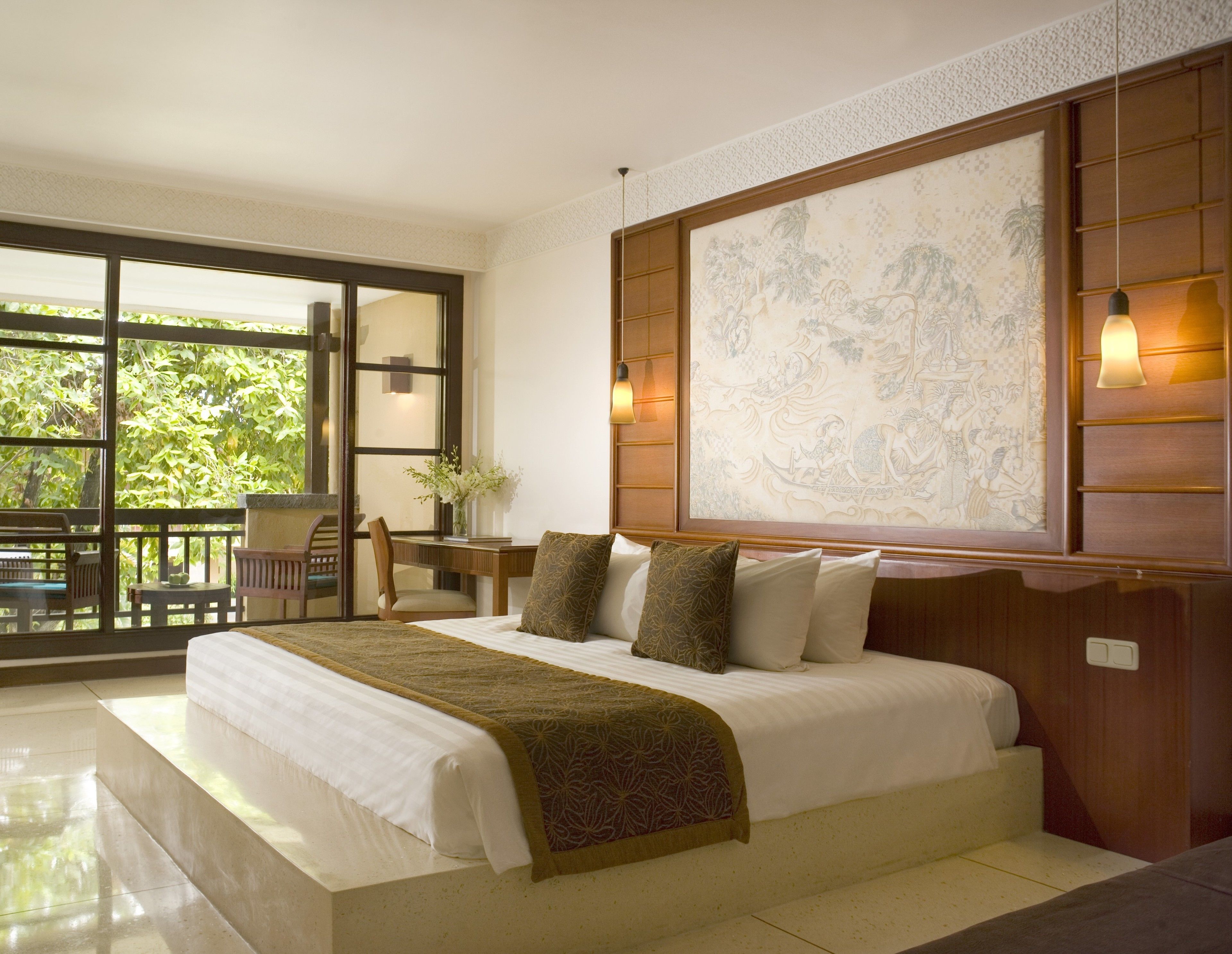 A hotel room with a large bed, a desk with a chair, a view of greenery outside, and a large decorative wall piece.