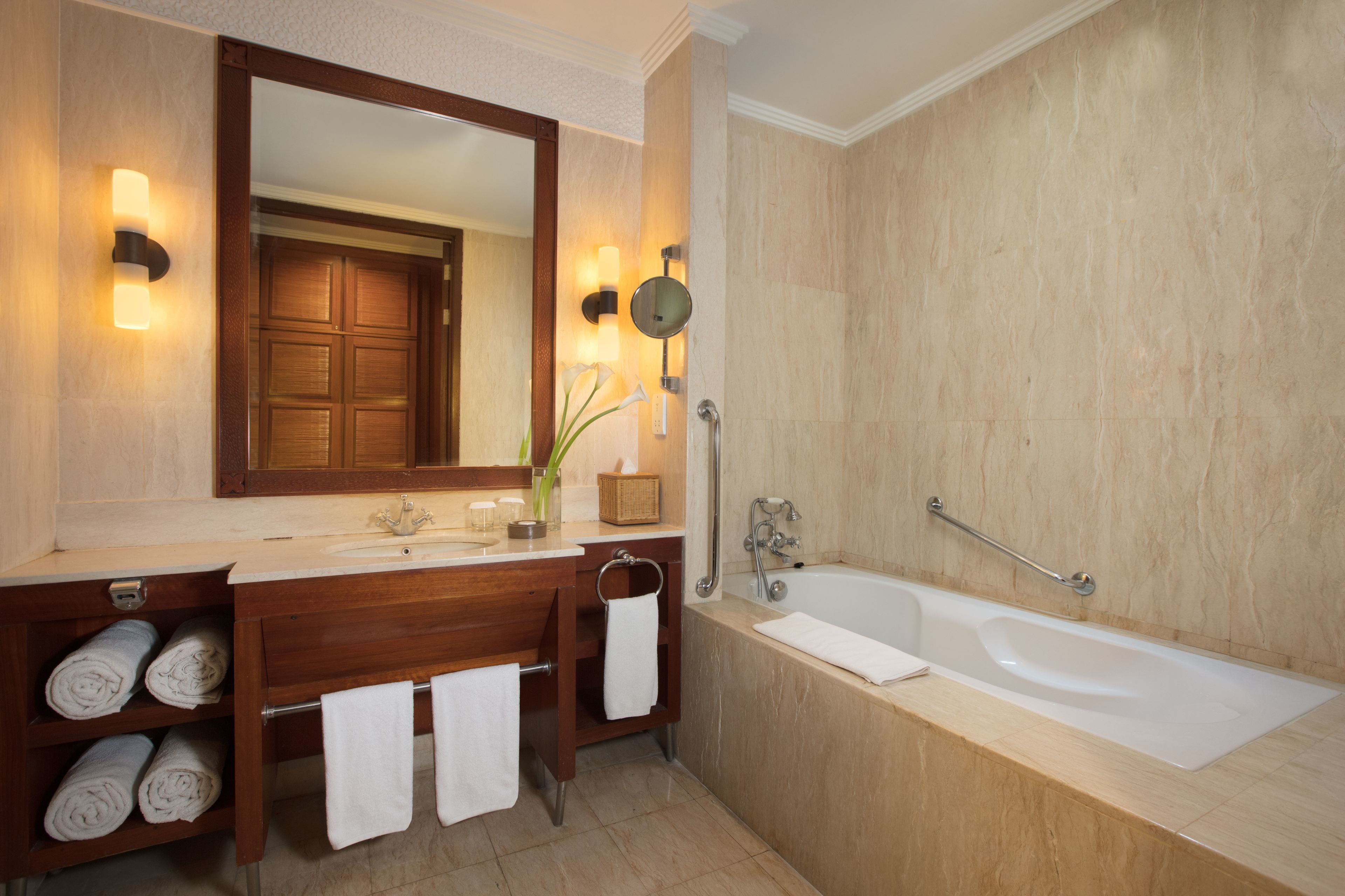 A modern bathroom with a large mirror, wooden vanity, multiple towels, a bathtub, and a handrail.