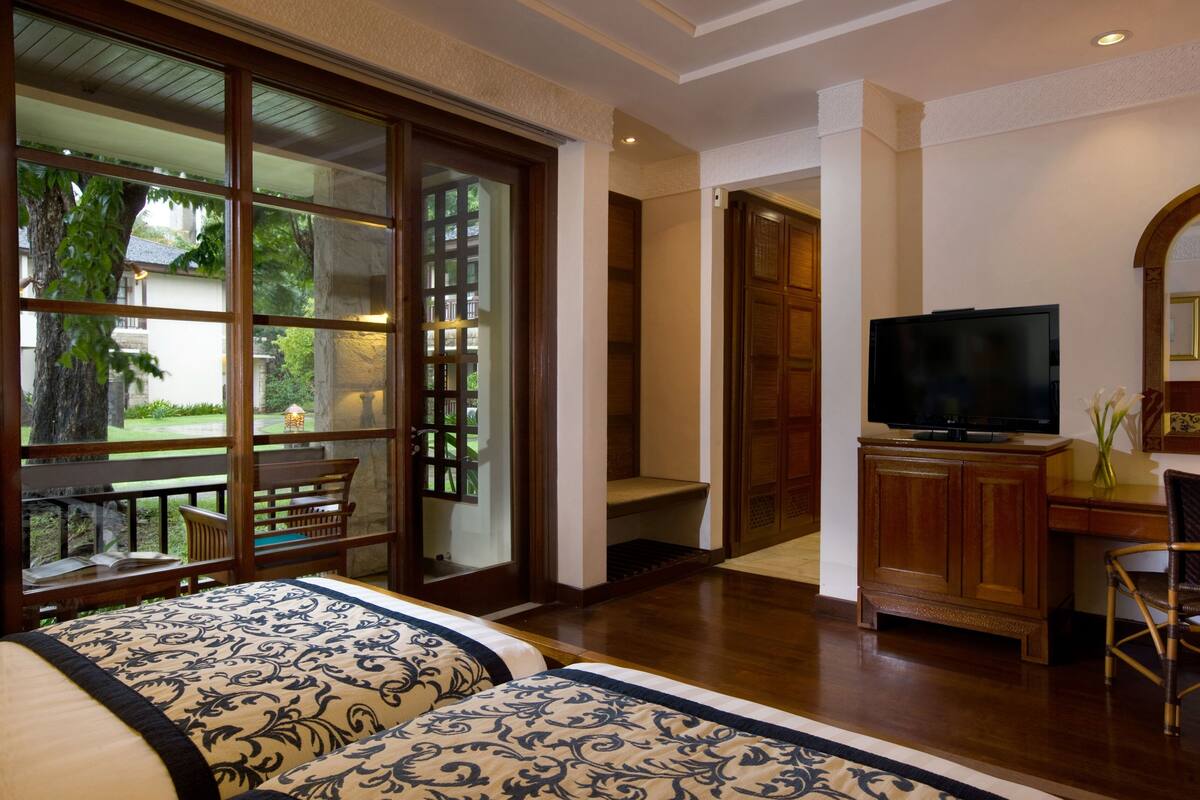 A hotel room with a large sliding glass door leading to a balcony, a bed with patterned bedding, a wooden desk with a television, and a chair.