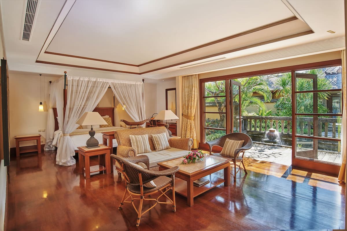 A spacious living room with a wooden floor, a sofa, a coffee table, and a view of a garden through large windows.