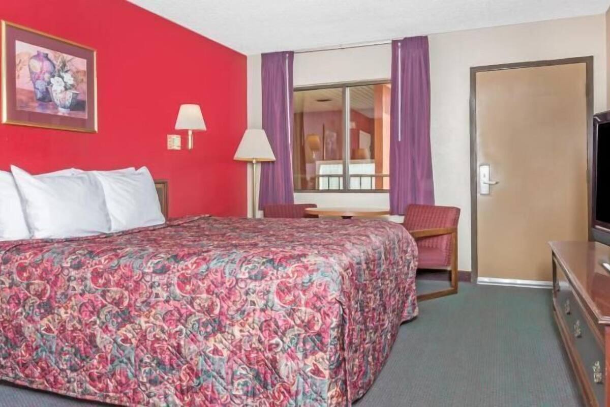 A hotel room with a bed, a desk, a chair, a TV, and a door.