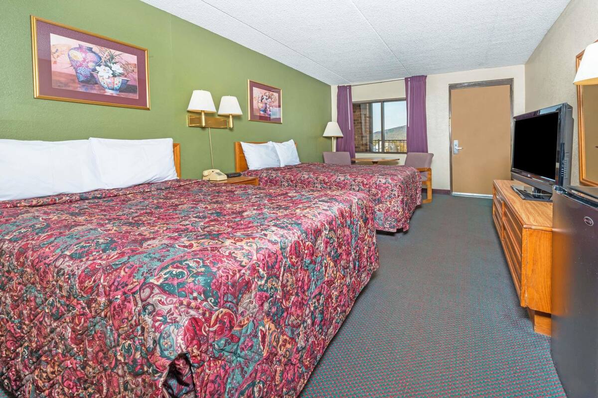A hotel room with two beds, a TV, a desk, and a window with a view.