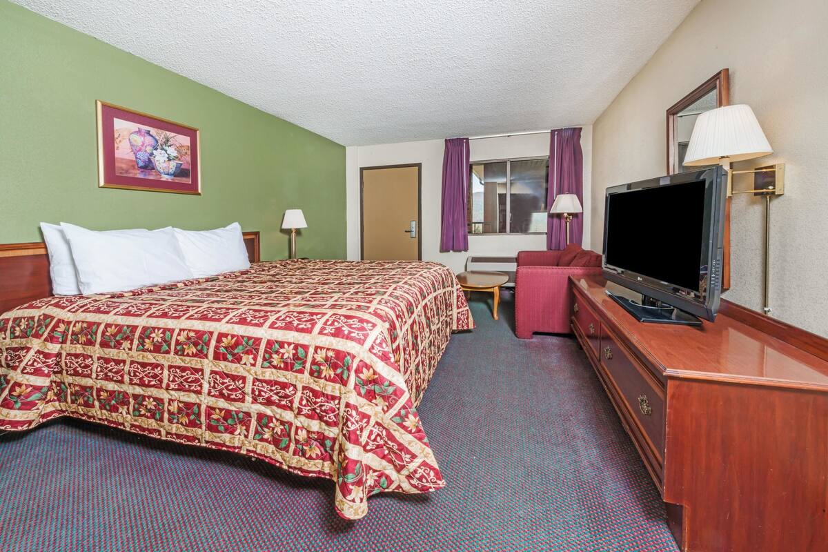 A hotel room with a large bed, a desk with a television, and a window with curtains.