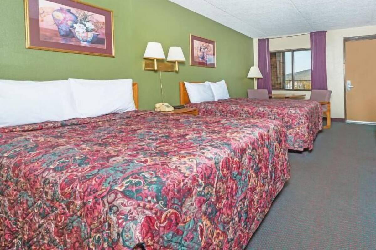 A hotel room with two beds, a television, a desk, and a window.