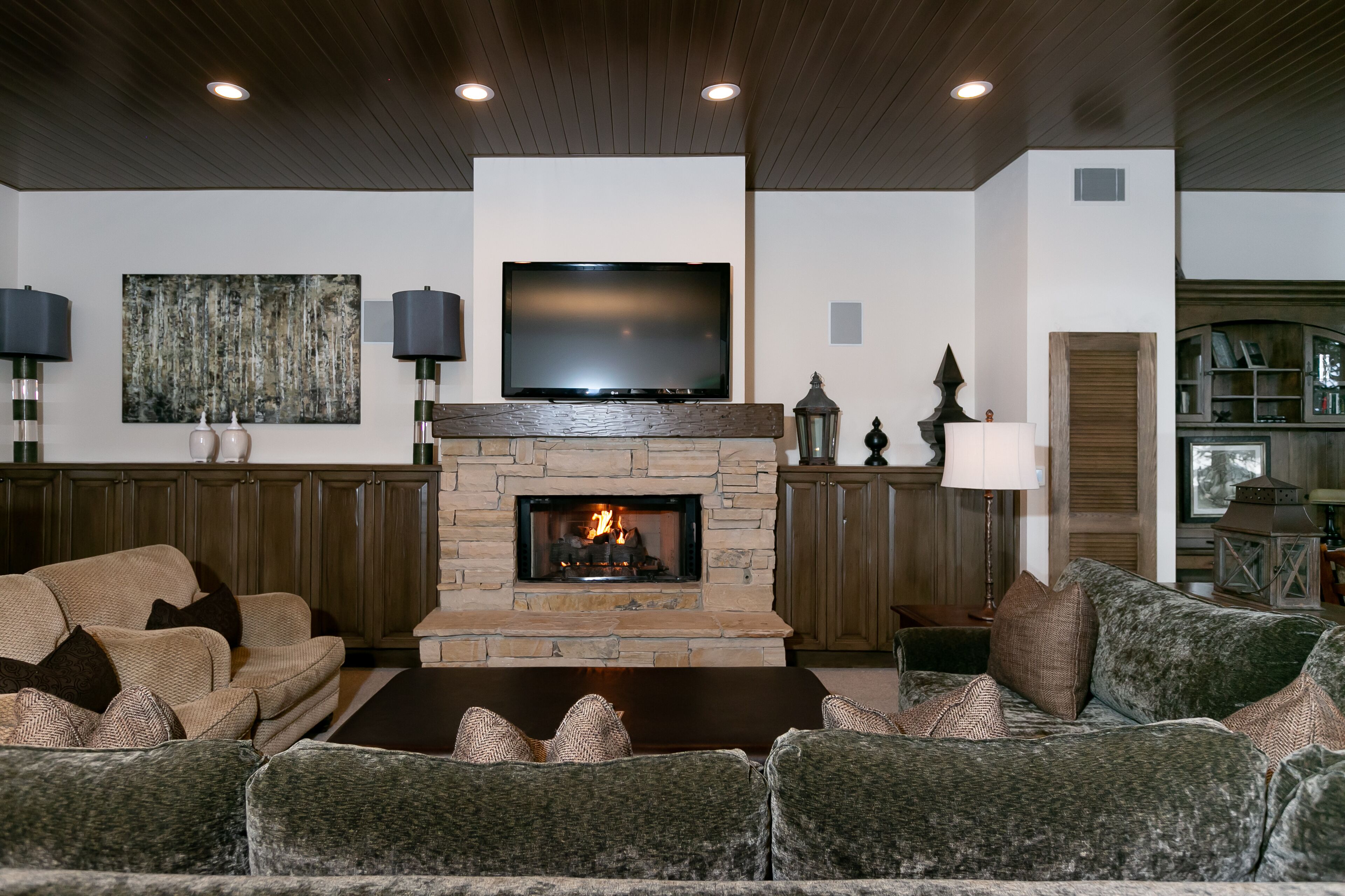 A living room with a stone fireplace, a flat-screen TV, and a large painting on the wall.