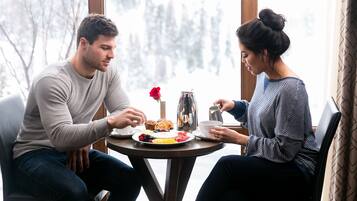 Two people sitting at a round table with a meal, a coffee pot, and a red rose.
