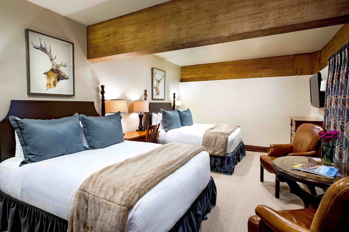 Ein Hotelzimmer mit zwei Betten, einer Holzbalkendecke und einem an der Wand montierten Fernseher.