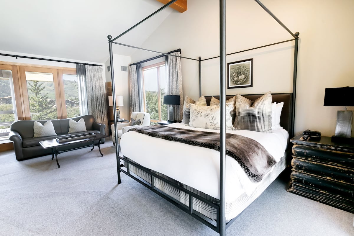 Ein Schlafzimmer mit Himmelbett, Sofa, Schreibtisch und Kommode, durchflutet von hellem Licht durch große Fenster.