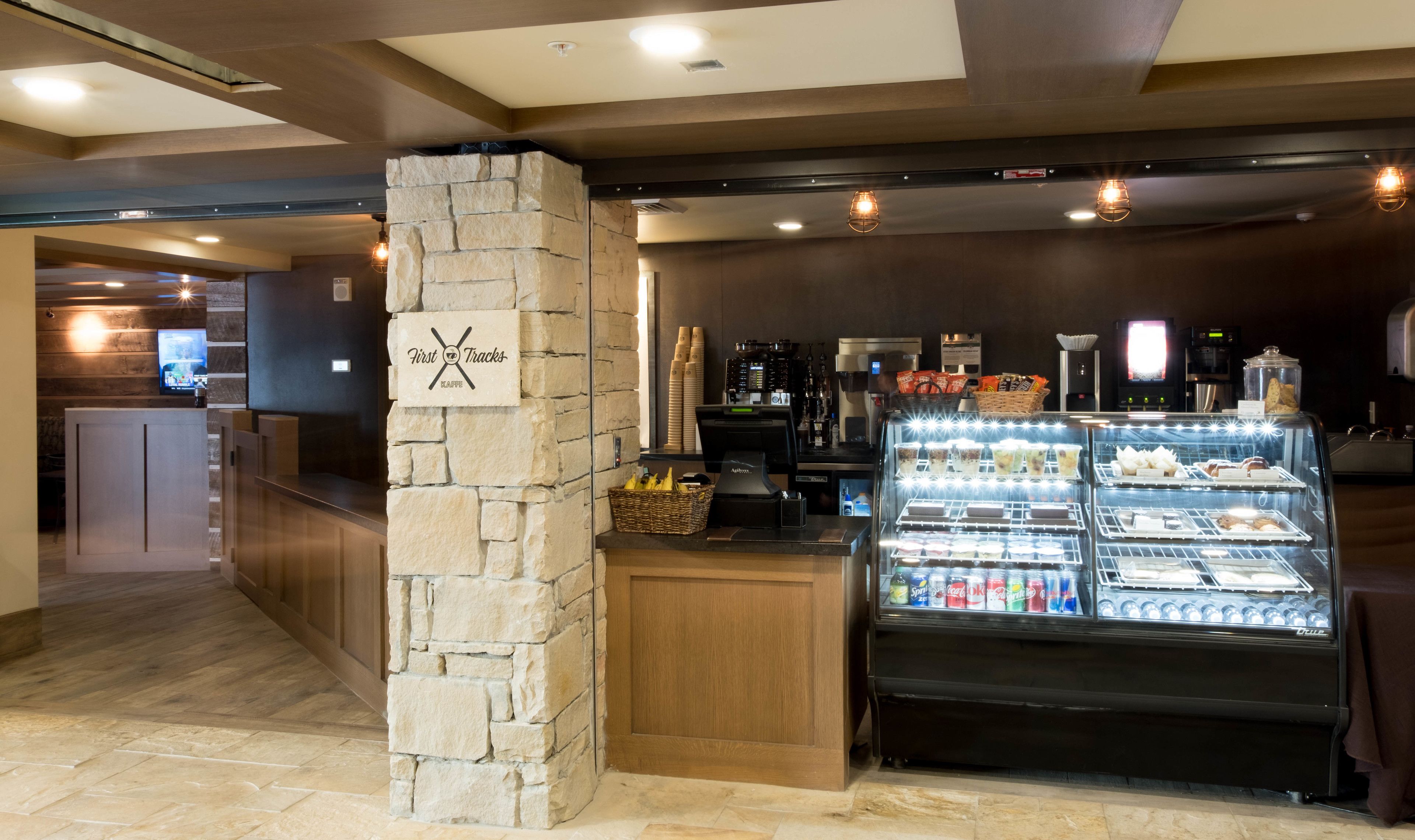 A cafe with a stone pillar, a coffee machine, and a display case with beverages.