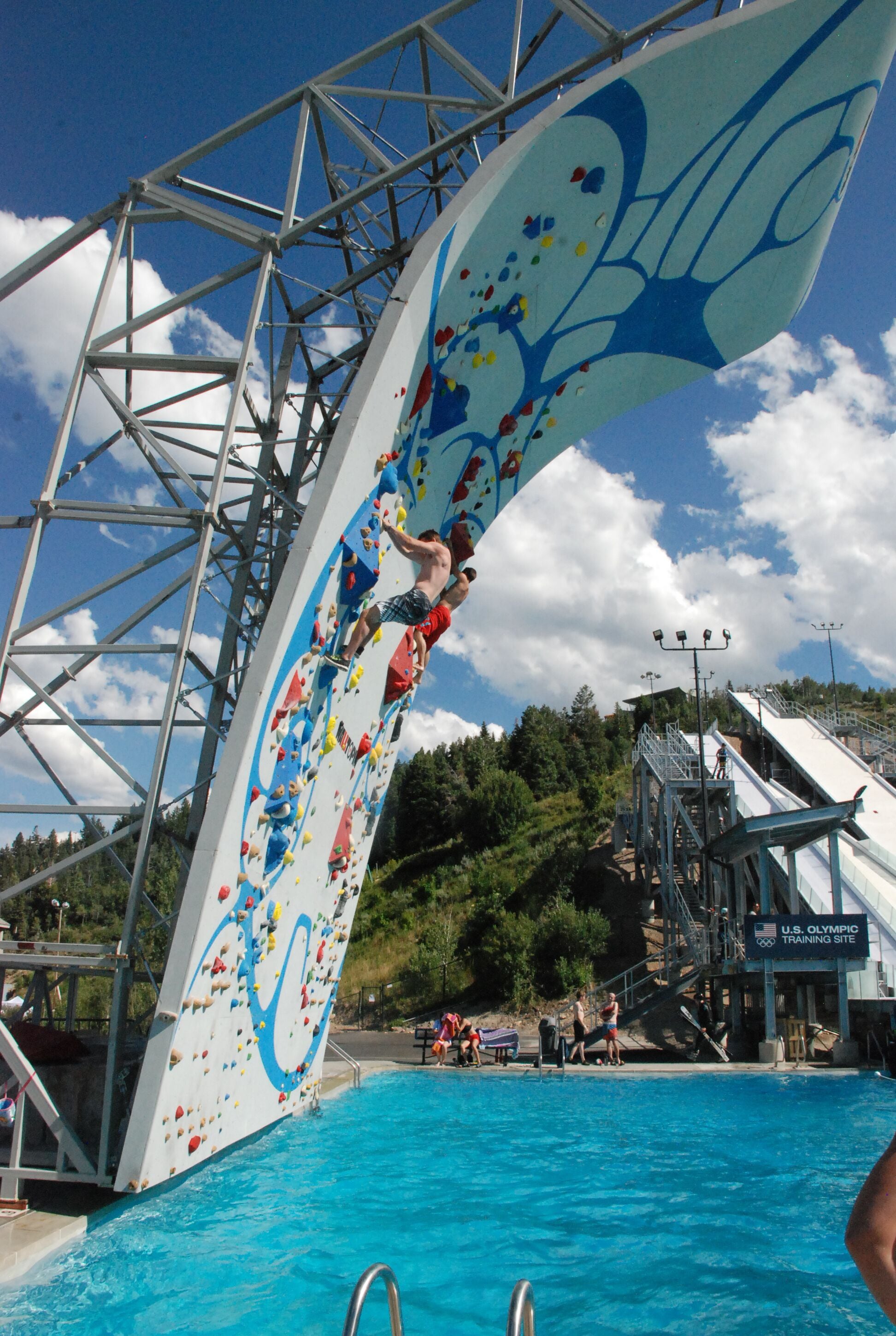 Eine Kletterwand mit farbenfrohem Design, ein Schwimmbecken und ein Schild mit der Aufschrift U.S. Olympic Training Site.