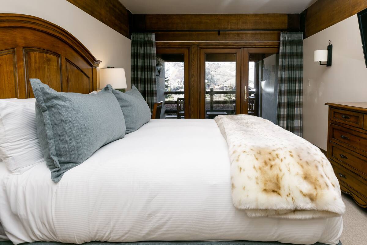 Ein Schlafzimmer mit einem großen Bett, einem Holzkopfteil, einem Nachttisch und Blick auf einen Berg durch eine Glastür.