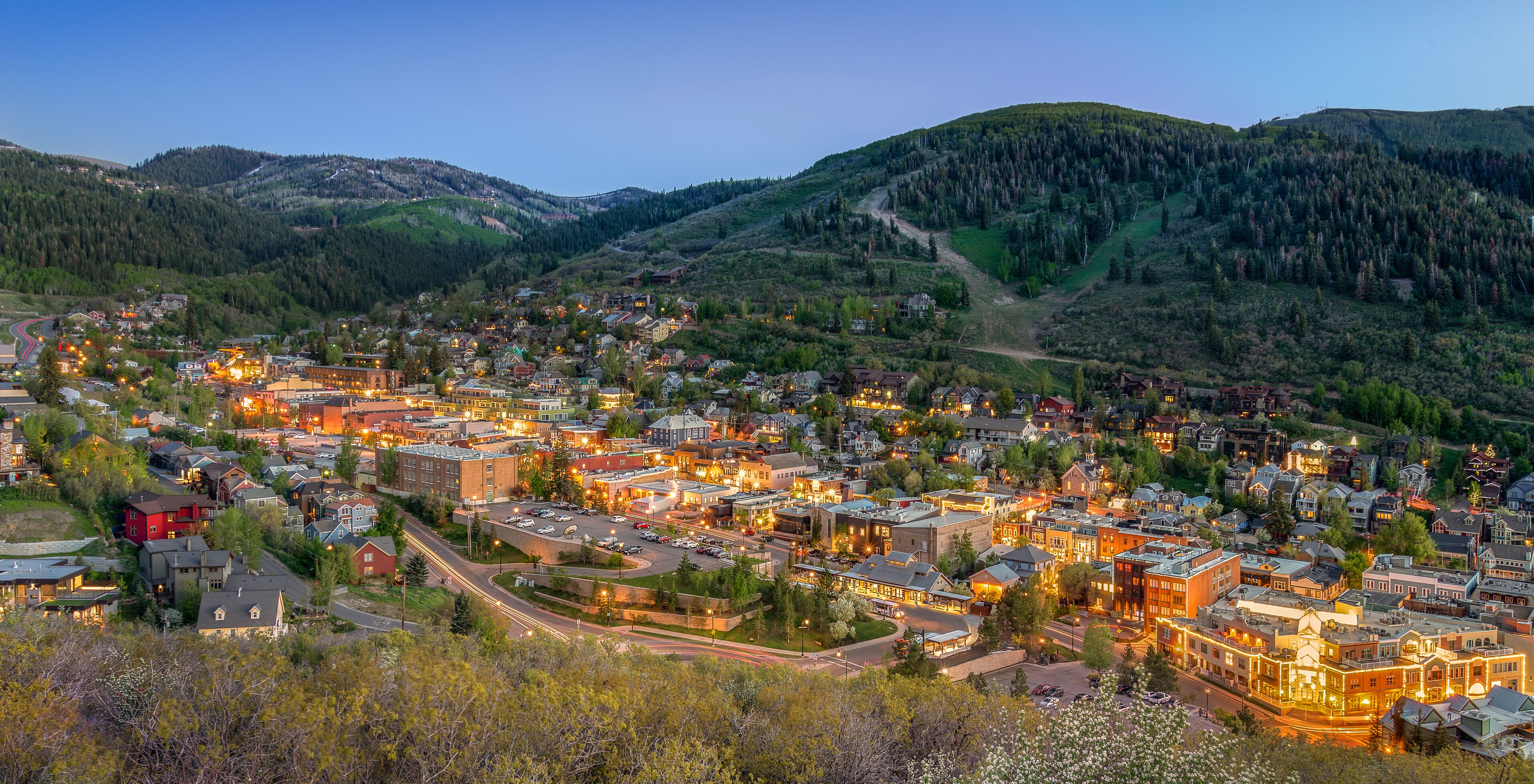 A town with a central square, surrounded by residential buildings and a mountain backdrop.