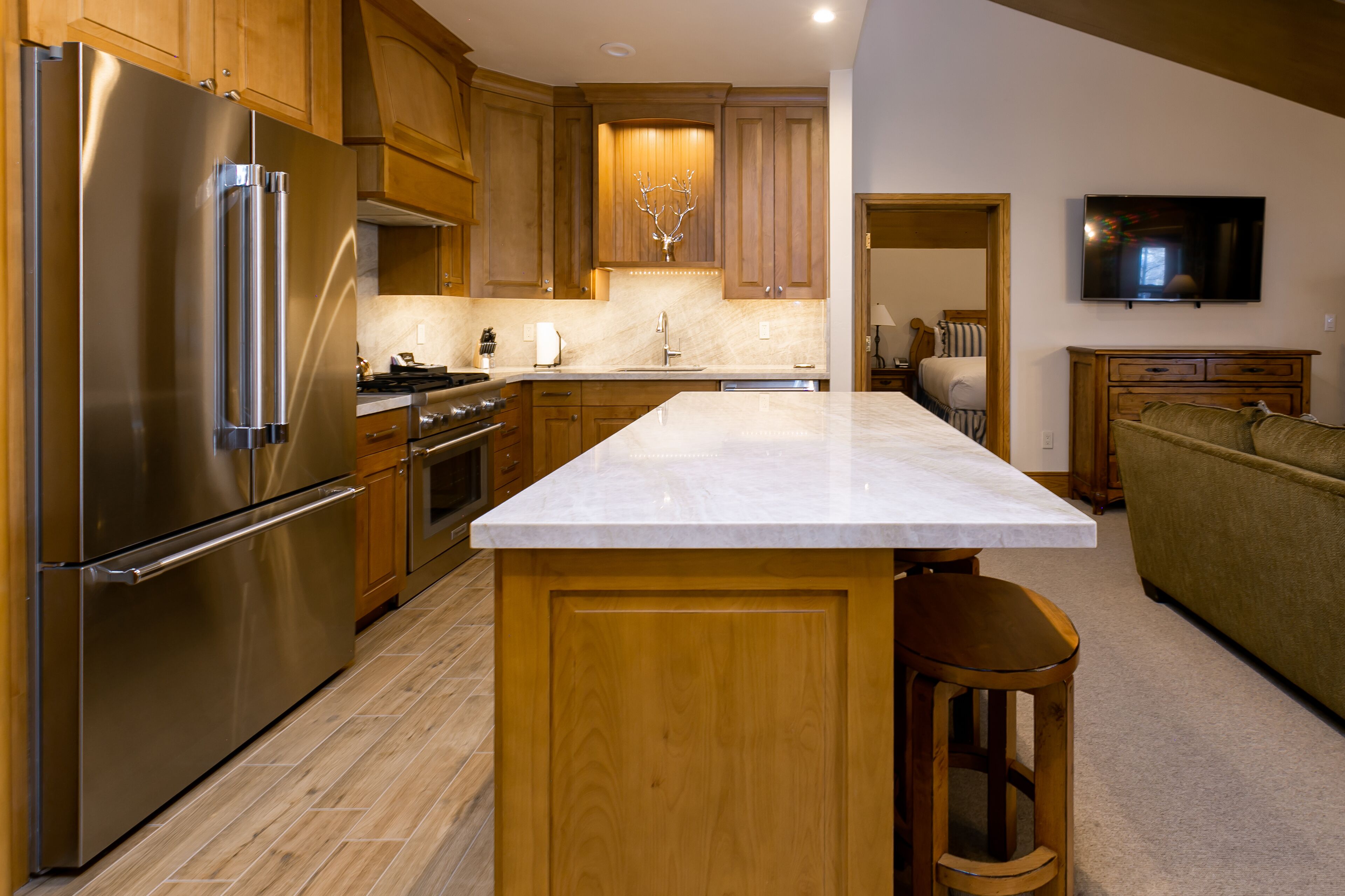 Una cocina moderna con armarios de madera, un refrigerador de acero inoxidable, una encimera de mármol y un televisor montado en la pared.