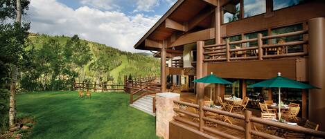 A large wooden building with a covered outdoor patio area, stone steps, and a grassy lawn.