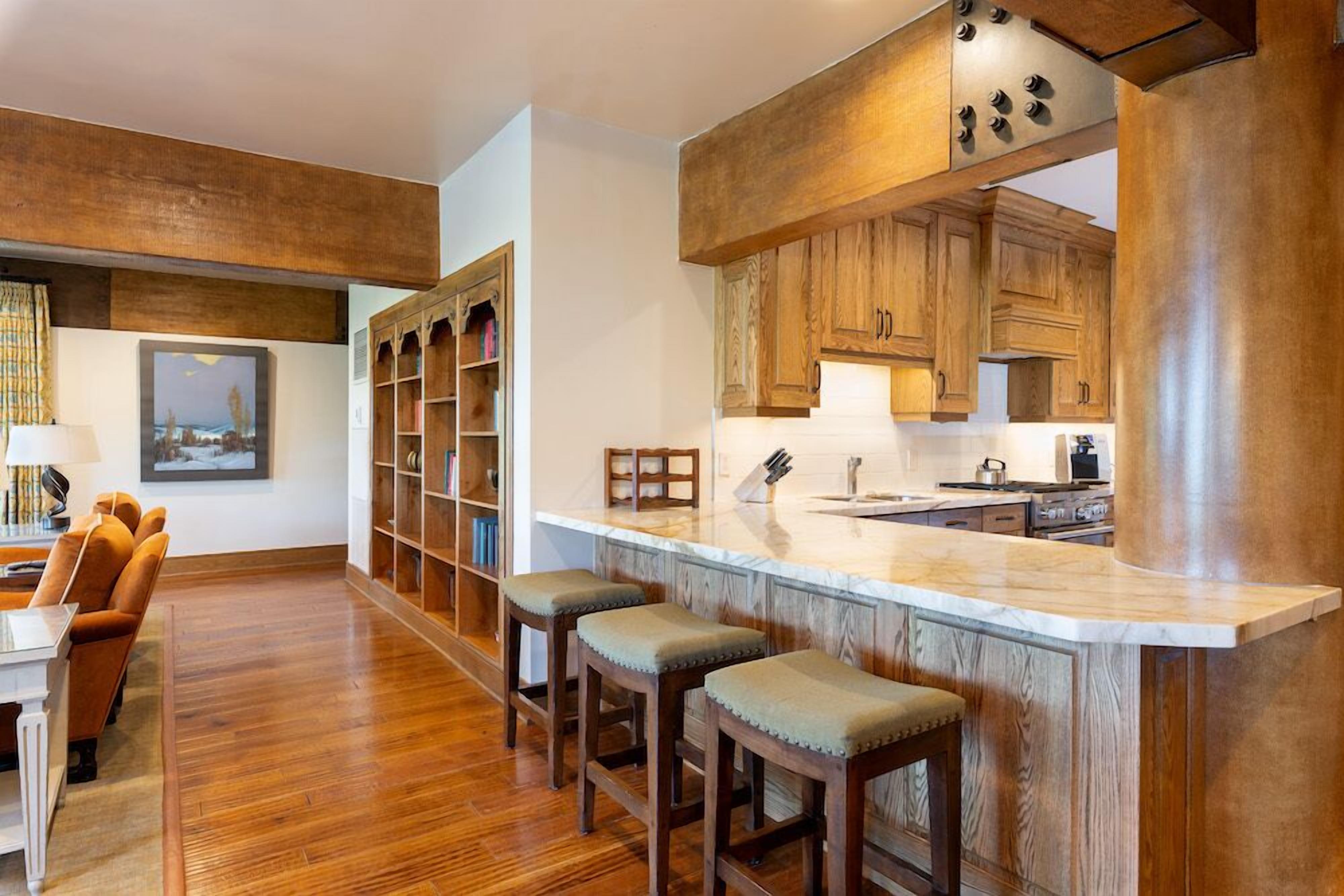A modern kitchen with wooden cabinets, a marble countertop, and bar stools.
