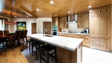 A modern kitchen with wooden cabinets, a marble island, and a dining area with a table and chairs.