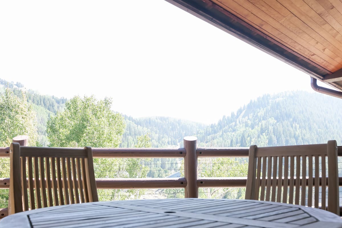 Eine Holzterrasse mit Tisch und Stühlen mit Blick auf ein bewaldetes Tal.