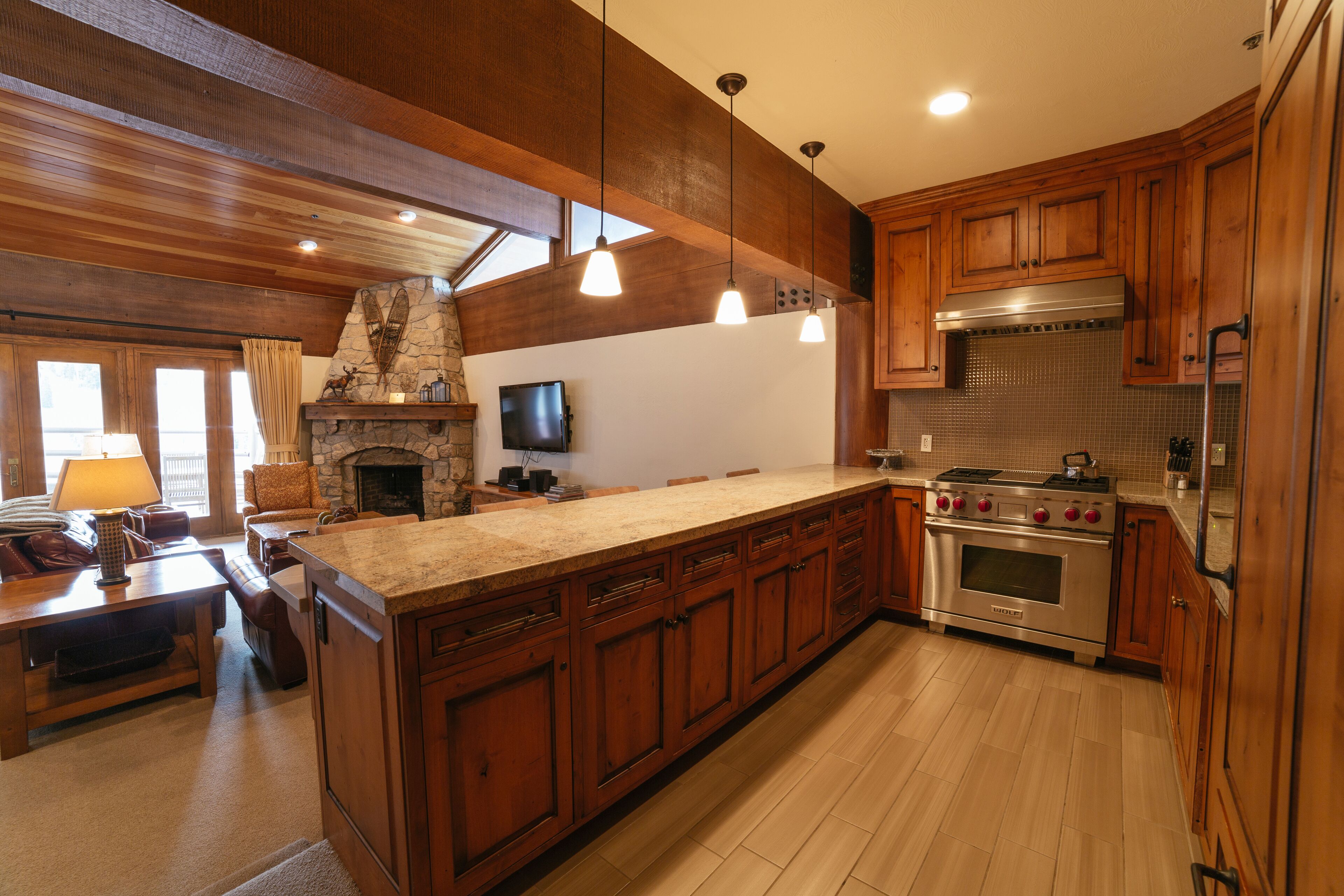 Une cuisine spacieuse avec des meubles en bois, un grand îlot central, une cheminée en pierre et une cuisinière moderne.