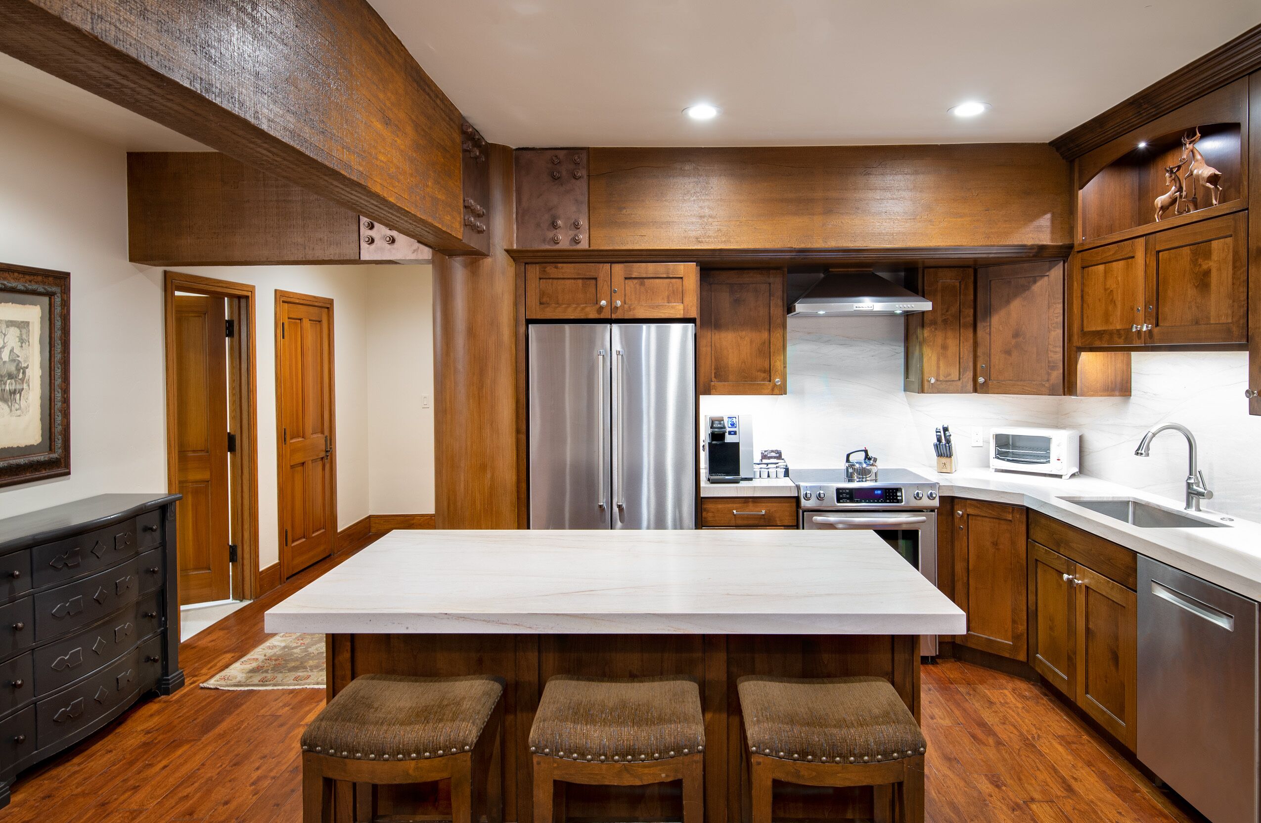 A kitchen with wooden cabinets, a stainless steel refrigerator, a white marble countertop, and a built-in oven.