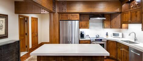 A kitchen with wooden cabinets, a stainless steel refrigerator, a white marble countertop, and a built-in oven.
