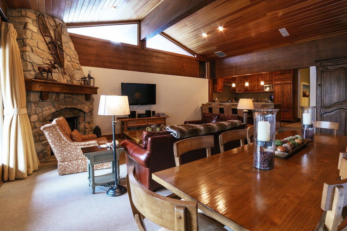 Ein geräumiges Wohnzimmer mit Kamin, Steinwand und Fernseher. Es gibt einen Essbereich mit Holztisch und Stühlen.