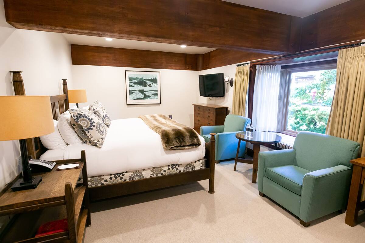 Ein Hotelzimmer mit Bett, Schreibtisch, Stuhl, Fernseher und einem Fenster mit Vorhängen.