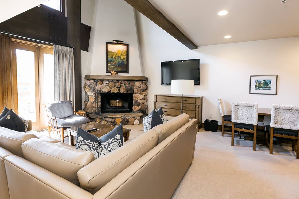 Ein Wohnzimmer mit Kamin aus Stein, einer Couch, einem Sessel, einem Fernseher und einem Tisch mit Stühlen.