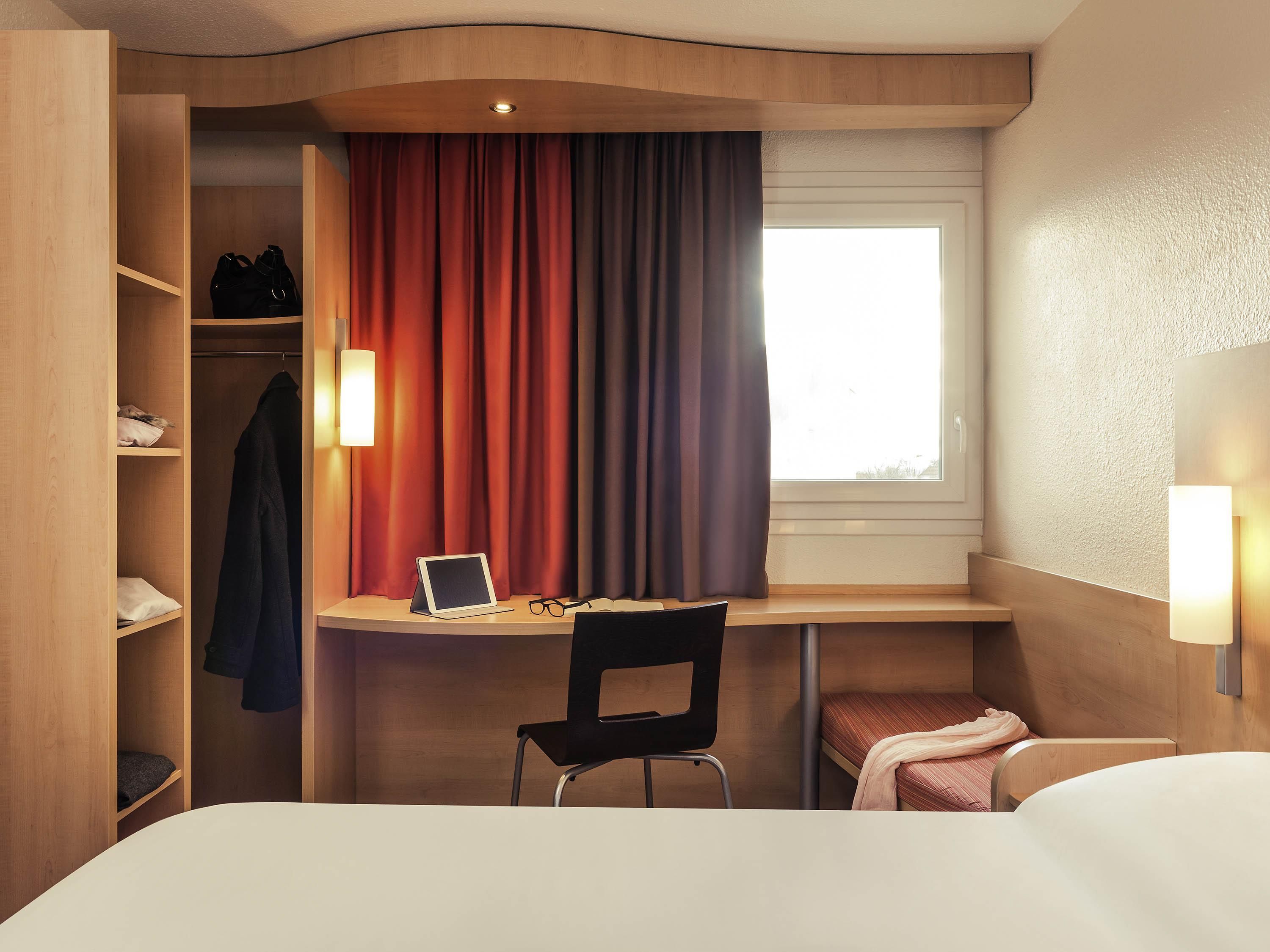 Une chambre d’hôtel de taille réduite, équipée d’un bureau, d’une chaise et d’un lit.