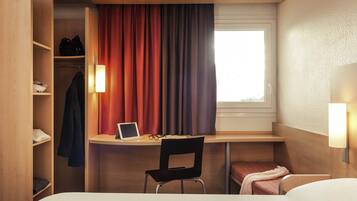 Une chambre d’hôtel de taille réduite, équipée d’un bureau, d’une chaise et d’un lit.