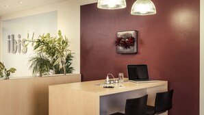 A reception desk with a laptop, a water bottle, and a glass. There are two black chairs and a potted plant. - ibis Epinay sur seine Gennevilliers (Epinay-sur-Seine)