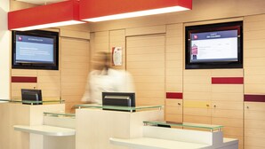A hotel reception area with glass partitions, digital screens displaying information, and a wooden panel wall. - ibis Epinay sur seine Gennevilliers (Epinay-sur-Seine)