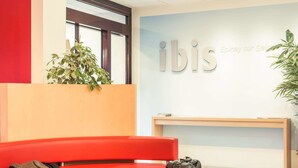 A red seating area with a table, a suitcase, and a plant. - ibis Epinay sur seine Gennevilliers (Epinay-sur-Seine)