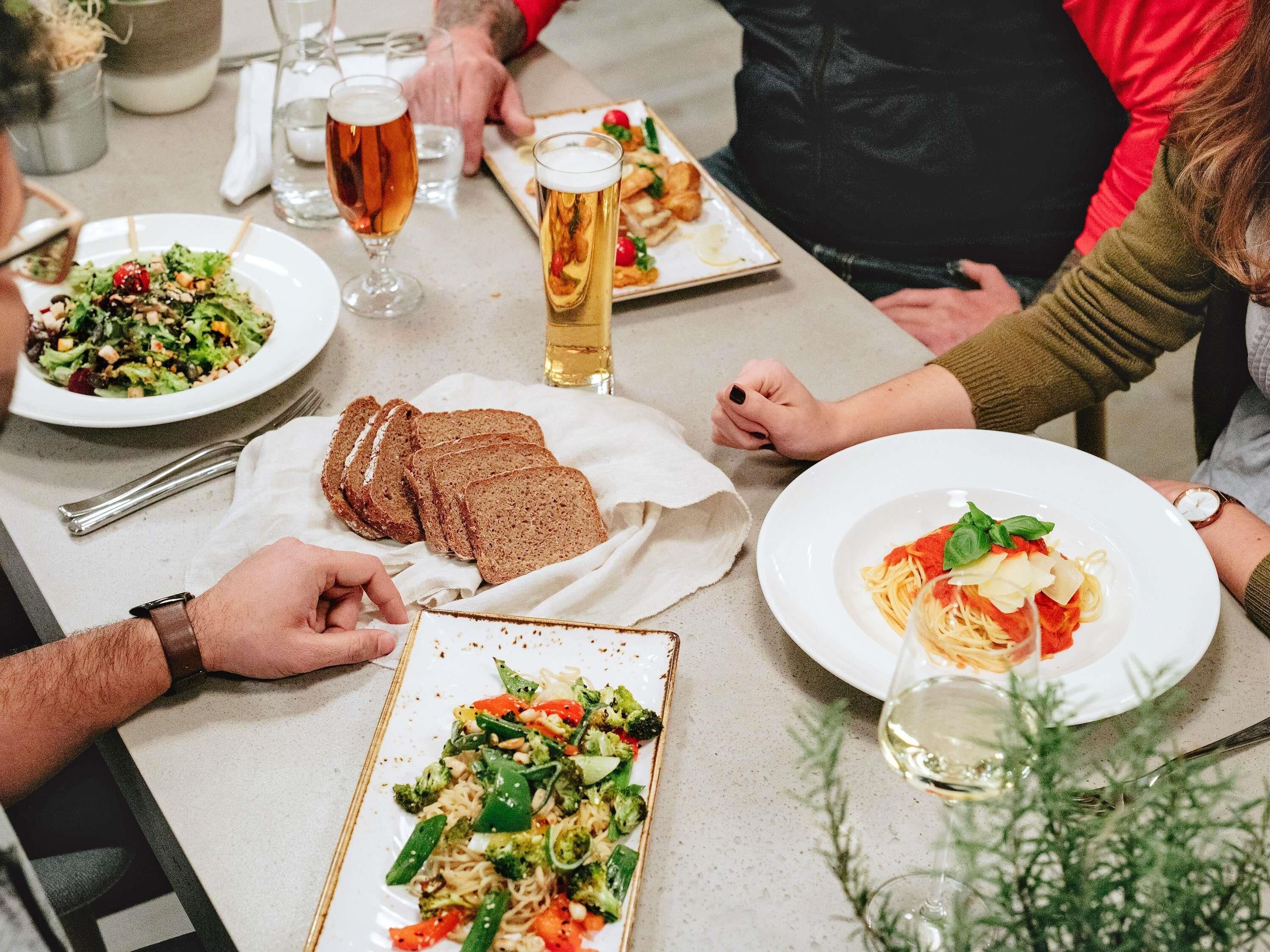 Una mesa de comedor con diferentes platos, vasos de cerveza y una persona con un reloj.