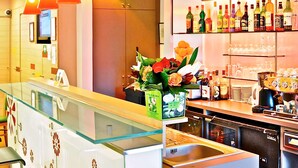 A hotel lobby with a reception desk, a glass partition, a flower arrangement, and a bar area with various bottles and glasses. - ibis Epinay sur seine Gennevilliers (Epinay-sur-Seine)