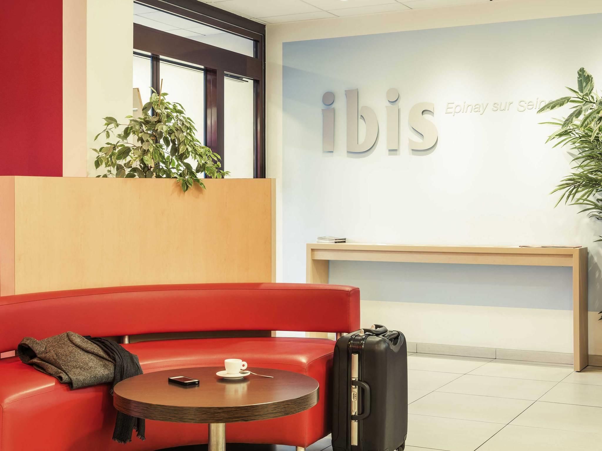 En röd sittgrupp med ett bord, en svart resväska och en skylt med texten ”ibis”.