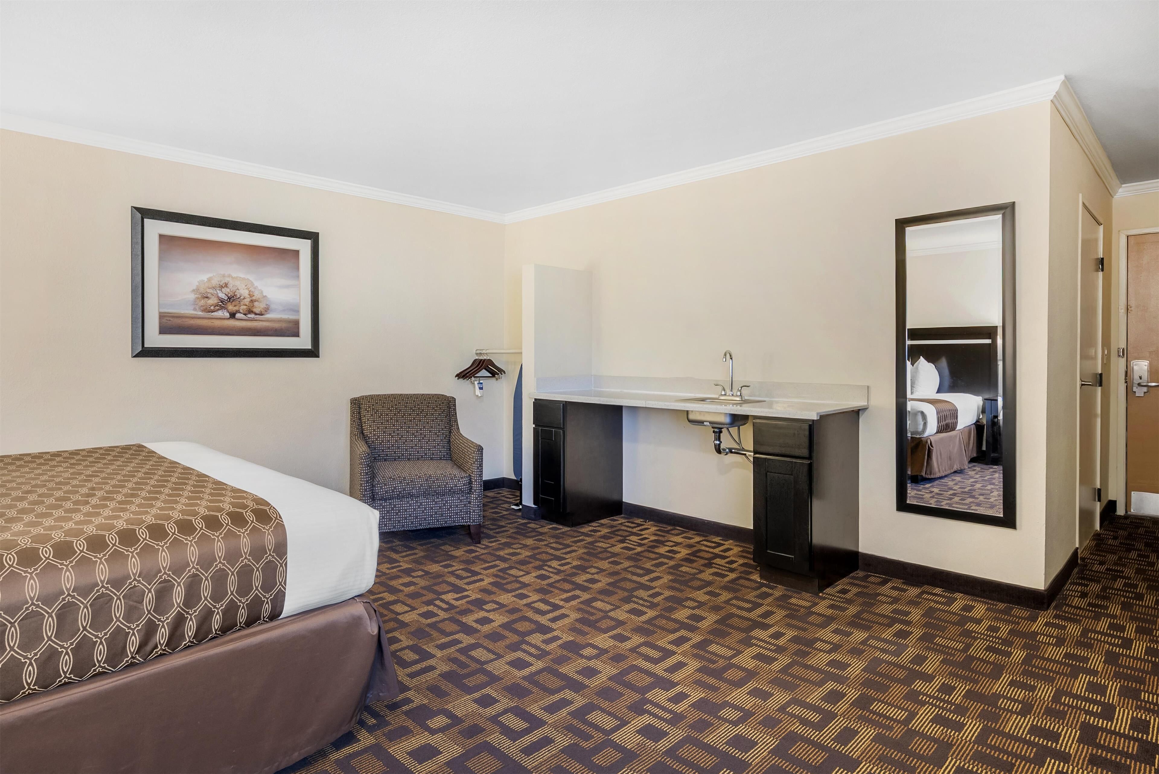 Ein Hotelzimmer mit einem Bett, einem Sessel, einem Schreibtisch mit Waschbecken und einem Spiegel.